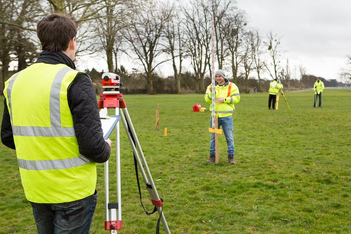 Trainees practising levelling with an optical level and staff in an open field